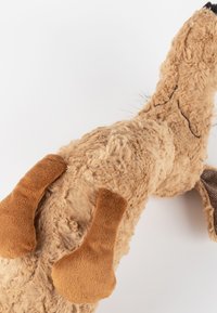 Tan plush toy with a textured, fuzzy body. It features brown, soft paw accents and subtle stitched details on the face and body.