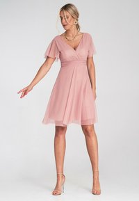 Jasnoróżowa sukienka z szyfonu, z krótkimi falbaniastymi rękawami, dekoltem w serek i dopasowaną talią, która przechodzi w spódnicę do kolan.