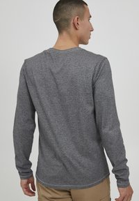 Langermet grå skjorte laget av teksturert stoff med rund hals og merkelapp på nederkanten. Har tettsittende ermer og et uformelt design.