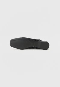 Black heeled sandal featuring a textured mesh upper, solid heel, and a patterned outsole with vertical grooves for traction.
