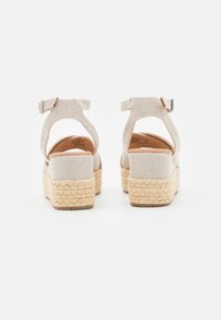 Sandales espadrilles beiges avec plateforme en jute tressé, bride de cheville et dessus en tissu texturé. Vue arrière, montrant la hauteur du talon et le détail de la bride.