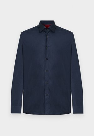 Chemise habillée à manches longues, bleu foncé, à boutons, avec col pointu, présentée à plat sur un fond blanc uni.
