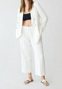 Witte getailleerde blazer en bijpassende cropped broek met een gladde textuur. Gecombineerd met een zwarte crop top en minimalistische witte sandalen.
