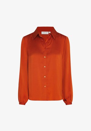Blouse en soie orange à manches longues, col pointu, boutonnage sur le devant et poignets froncés sur fond blanc.