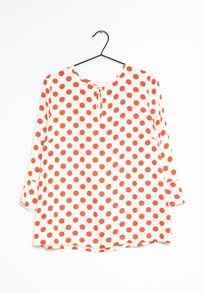 Blusa a maniche lunghe color crema con grandi pois rossi. Presenta un colletto rotondo e una piccola bottoniera sul davanti. Tessuto morbido.