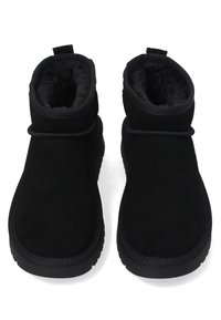 Een paar zwarte suède winterlaarzen met een zachte fleece voering en dikke rubberen zolen, van bovenaf gezien op een witte achtergrond.