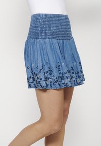 Denim szoknya ráncolt derékpánttal, hímzett virágmintákkal kék és ezüst színben az alján. Bővülő forma és könnyű anyag.