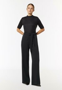 Black short-sleeve top with a high neckline paired with high-waisted, wide-leg black trousers, featuring a tied belt detail.