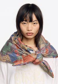 Pañuelo de seda multicolor con un patrón repetido de animales y flores, anudado de manera suelta alrededor del cuello. Textura suave con un acabado brillante.