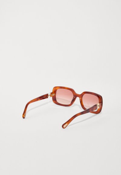 Lunettes de soleil en écaille de tortue marron avec des montures carrées, des verres roses et des accents en métal doré. Équipées de branches lisses et courbées pour un ajustement confortable.
