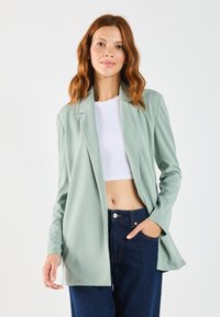 Light green blazer made of soft fabric with a tailored fit, open front, and long sleeves, paired with a white crop top and dark denim pants.