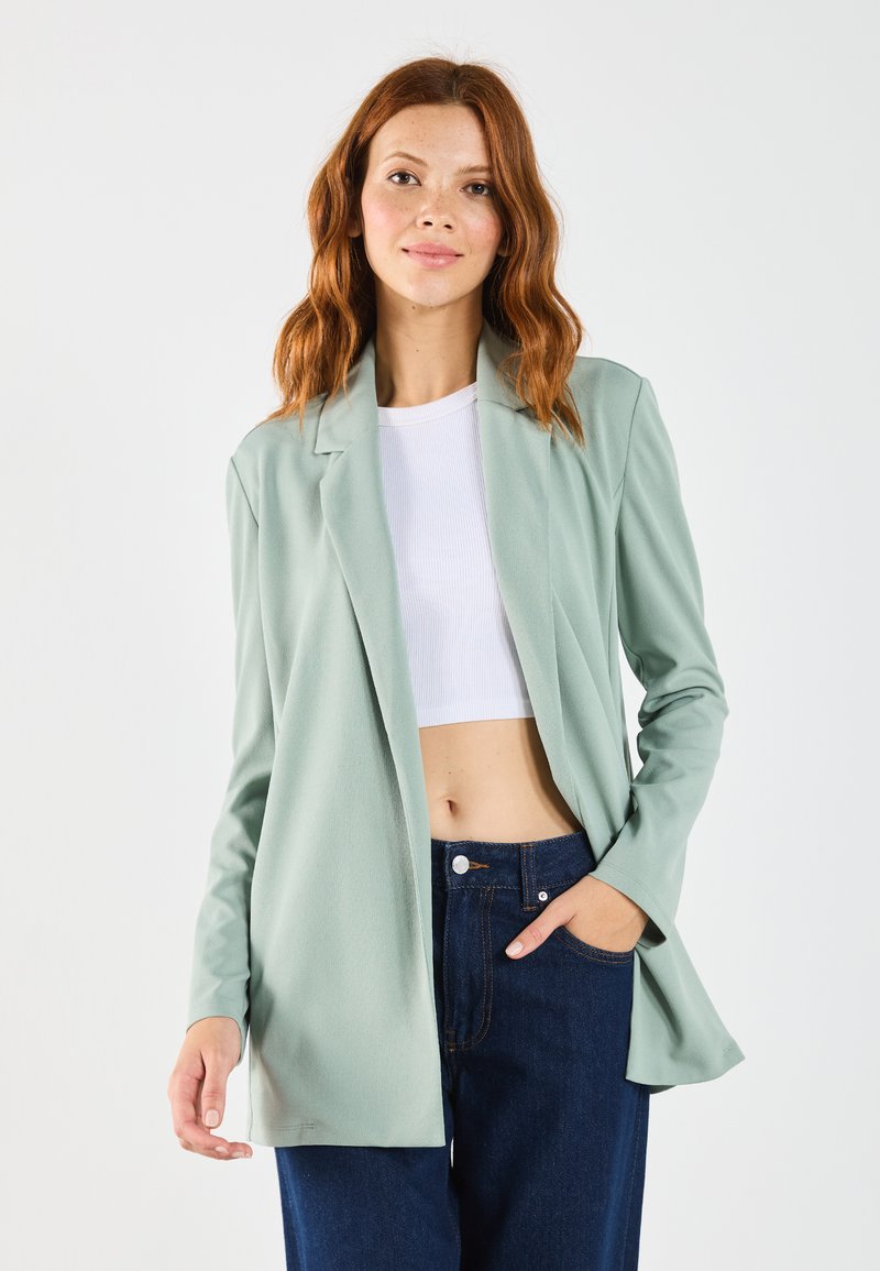 Light green blazer made of soft fabric with a tailored fit, open front, and long sleeves, paired with a white crop top and dark denim pants.