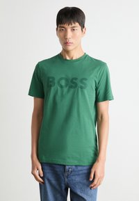Zöld pamut póló kerek nyakkivágással és rövid ujjakkal, a mellkason egy nagy, sötétzöld "BOSS" logóval.