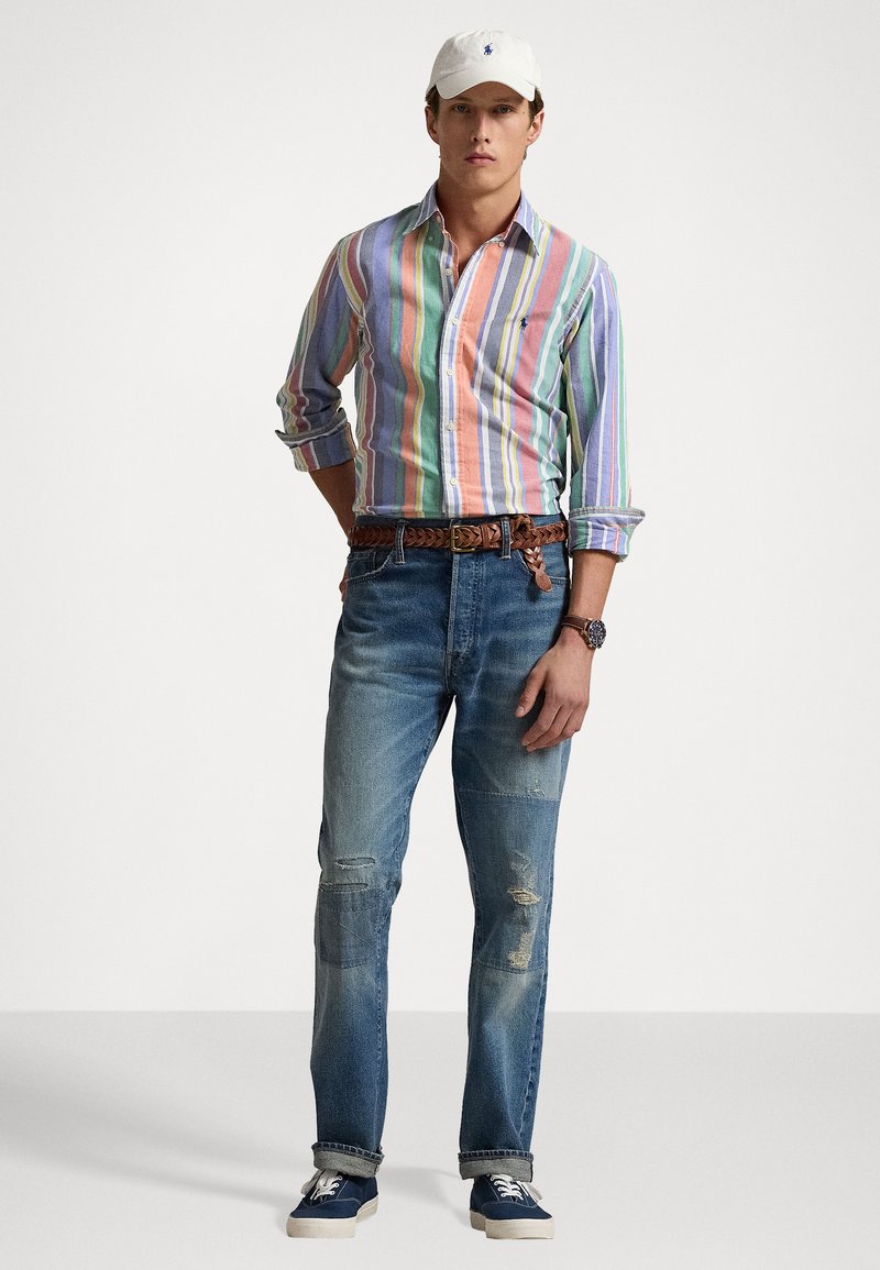 Gestreiftes Hemd in Pastellfarben, ausgebleichte blaue Jeans, geflochtener brauner Gürtel, weiße Kappe und marineblaue Sneakers. Lässiger und bequemer Schnitt.