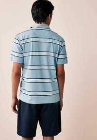 Camisa polo de manga corta azul claro con rayas horizontales en marino y blanco, hecha de una tela suave; combinada con pantalones cortos oscuros.