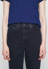 Mörkblå högmidjade jeans med en slät yta, med dragkedja, två framfickor och synlig sömnad längs sömmarna.