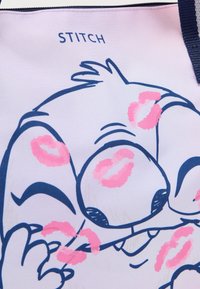 Τσάντα tote με σχέδιο χαρακτήρα, ροζ αποτυπώματα φιλημάτων, μπλε περιγράμματα και το κείμενο «STITCH», σε ανοιχτό ροζ φόντο.