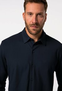 Camicia a manica lunga blu navy con frontale con bottoni, colletto a punta e logo discreto sul petto. Tessuto morbido, vestibilità sartoriale, senza fantasie.