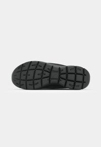 Black rubber shoe sole featuring a textured grip pattern with prominent treads and grooves for enhanced traction and stability.