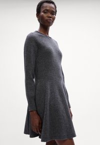 Abito lavorato a maglia grigio con maniche lunghe, scollatura rotonda e gonna svasata. Il tessuto appare morbido, con una consistenza liscia e dettagli delicati.
