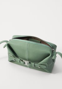 Borsa a pochette verde in pelle con chiusura a cerniera, caratterizzata da una superficie testurizzata, dettagli cuciti e un grande fiocco in evidenza sulla parte anteriore.