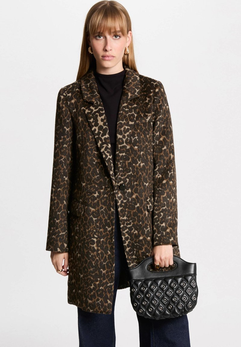 Cappotto maculato con tonalità marroni e beige, colletto strutturato e due tasche frontali. Borsa nera con design trapuntato e manico.