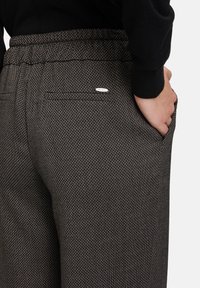 Gewebte, gemusterte Hose in Dunkelbraun und Schwarz, mit einer lockeren Passform, elastischem Bund und einem kleinen Logo-Tag über der Gesäßtasche.