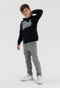 Felpa nera con cappuccio e grafica "Utah", pantaloni grigi e sneakers bianche. Il tessuto è morbido e la vestibilità è rilassata, con una tasca frontale.