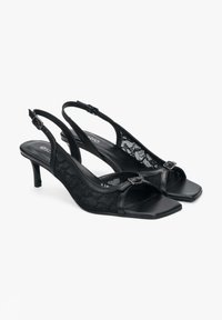 Czarne czółenka na obcasie typu slingback z koronkowym wykończeniem, kwadratowym noskiem, regulowanym zapięciem oraz fakturowaną wkładką, z niskim obcasem.