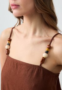 Braunes Leinenkleid mit dicken Trägern, das farbenfrohe Holzkugeln in verschiedenen Formen und Größen aufweist. Strukturiert textiles Material mit seitlicher Raffung.