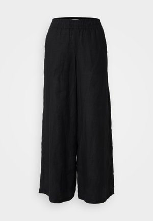 Černé široké kalhoty vyrobené z lnu s elastickým pasem. Tkanina má matnou strukturu a volně splývá od pasu až po kotníky.