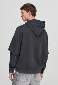 Felpa grigia con una vestibilità ampia, con un grande cappuccio, spalle scese e polsini a coste, realizzata in un morbido tessuto testurizzato.