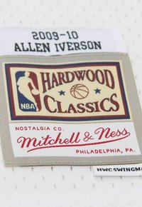 L'etichetta in tessuto di Mitchell & Ness presenta il logo 'Hardwood Classics' in rosso e blu, con '2009-10 Allen Iverson' in nero su uno sfondo grigio.