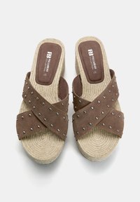 Sandali slip-on in suede marrone con cinturini incrociati, caratterizzati da borchie argentate e una suola in stile espadrilles tessuta e testurizzata.