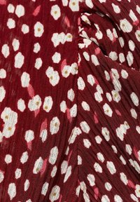 Röd texturerad tyg med ett blommönster som har vita och rosa blommor med gula mittpunkter. Designen har ett lätt och svävande utseende.