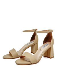 Sandali con tacco alto aperti beige, con una larga cinghia anteriore e cinghia alla caviglia, caratterizzati da un tacco a blocco e una texture in pelle liscia.