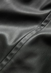 Schwarzer Kunstlederstoff mit glatter Textur und dezentem Glanz, der eine genähte Naht aufweist, die der Oberfläche Detail verleiht.
