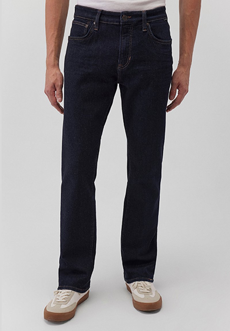 Dunkelblaue Jeans aus Denim mit geradem Schnitt, Fünf-Taschen-Design, sichtbaren Nähten und normaler Taillenhöhe. Kombiniert mit beigen Sneakers.
