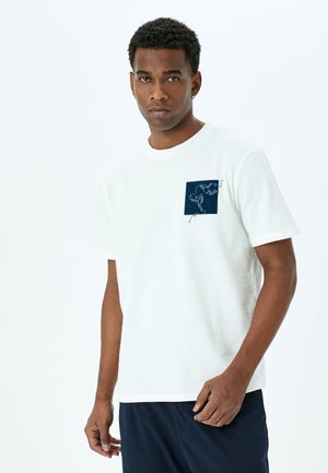 White cotton t-shirt with a crew neckline, featuring a navy square patch with a line drawing design on the left chest area. Short sleeves.