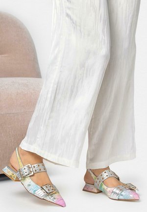 Femeie purtând pantaloni albi, largi, cu textură, și pantofi colorati metalici, ascuțiți, cu bretele și catarame, cu toc bloc jos.