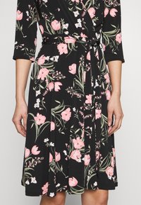 Schwarzes Kleid mit floralem Muster in pinken Tulpen und grünen Blättern, mit Dreiviertelärmeln und einem Taillengurt für eine verstellbare Passform.