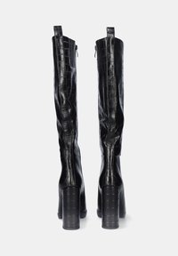 Botas negras hasta la rodilla, hechas de un material brillante y texturizado con un patrón de cocodrilo, que cuentan con un tacón grueso y cierre de cremallera en el lado.