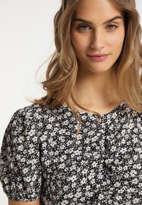 Sort og hvid blomstret bluse med puffede ærmer, flæsedetaljer og rund udskæring, lavet af letvægtigt stof.