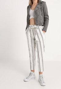 Gray suede biker jacket over a white crop top, paired with white striped pants and gray high-top sneakers. Front view, standing posture.