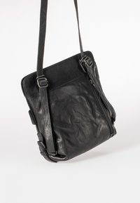 Borsa a tracolla nera in pelle con una texture liscia, cinturino regolabile e chiusura a zip visibile. Presenta un design minimalista e una costruzione robusta.