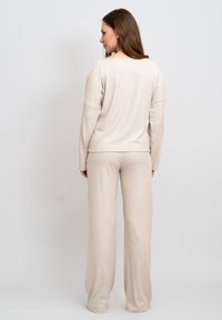 Beige Lounge-Set bestehend aus einem Langarmoberteil und lockeren Hosen. Weicher Stoff, entspannte Passform mit einem dezenten Rippenmuster.