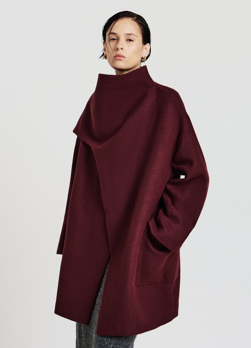 Burgunderroter Wollmantel mit hohem Kragen, oversized Schnitt, seitlichen Taschen und einem gewickelten Frontdesign, das eine glatte Textur aufweist.