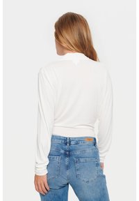White long-sleeve top with a fitted design, ribbed texture, crew neckline, and a cropped cut, paired with high-waisted blue denim jeans.