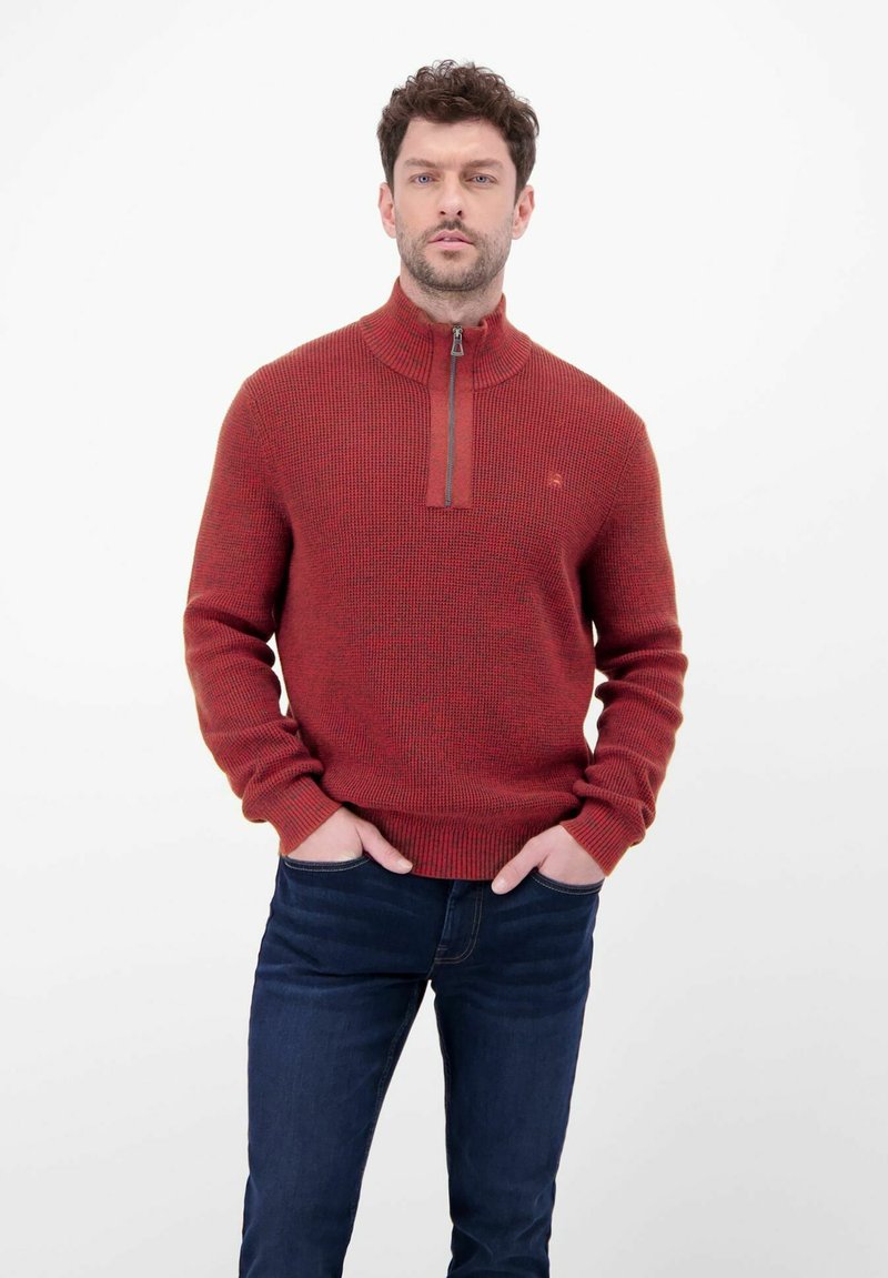 Roter, strukturierter Pullover mit hohem Kragen und Reißverschluss, getragen über dunklen Jeans. Schmale Passform mit gerippten Bündchen und Saum.