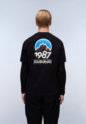 Black cotton t-shirt featuring a colorful mountain graphic with a blue sky and "1987" text, along with "Napapijri geographic" branding below.